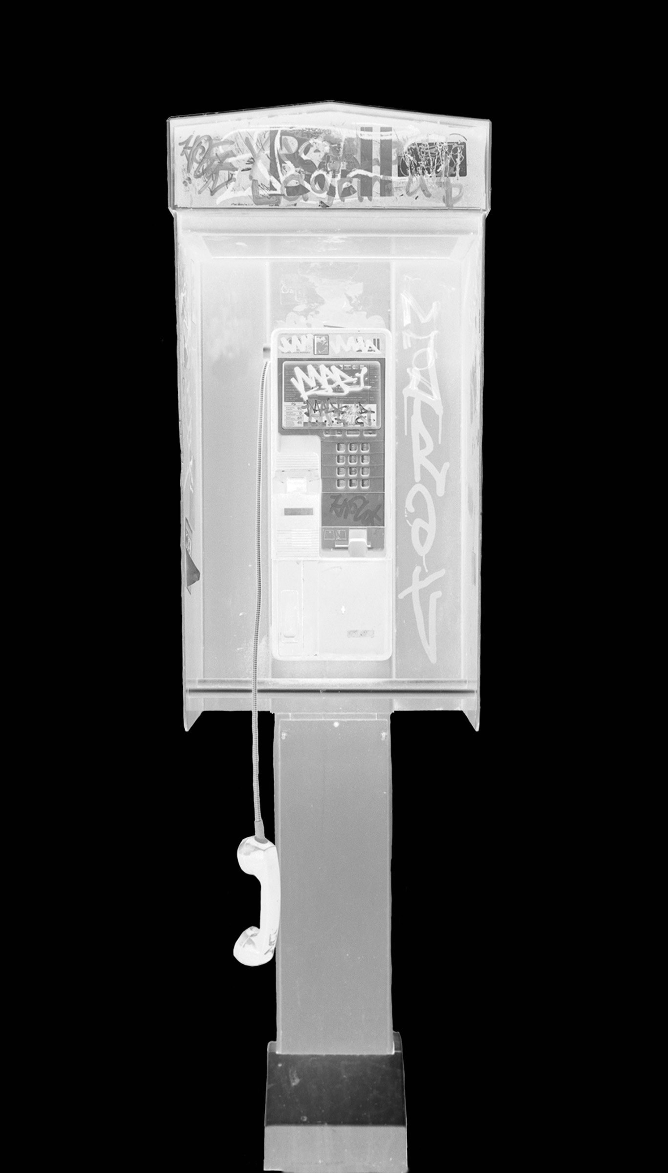 A black and white photo of a pay phone with a thick black border around it. The payphone has graffiti on the top and sides around the phone. The phone is hanging down off its stand by the cord.