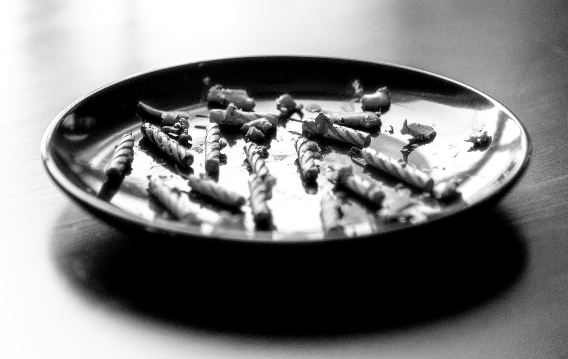 A black and white photo of a plate on a table. On the plate are 13 striped candles that have been partially melted.