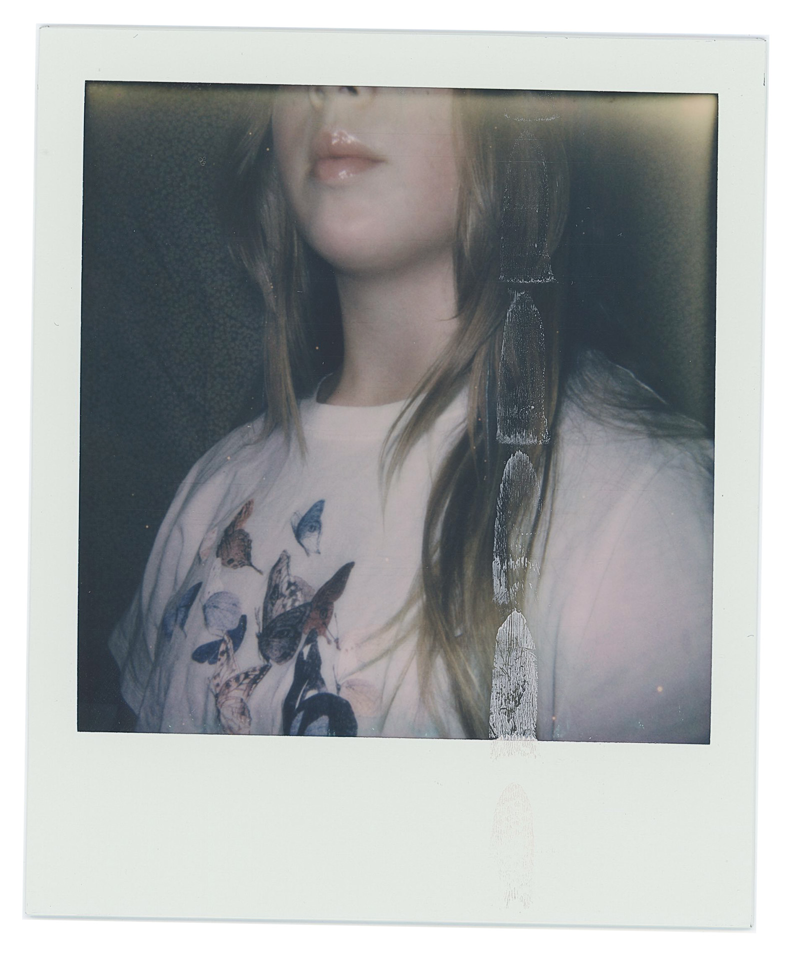 A Polaroid of Eden, from her nose to her chest. She is wearing a white t-shirt with butterflies on it.