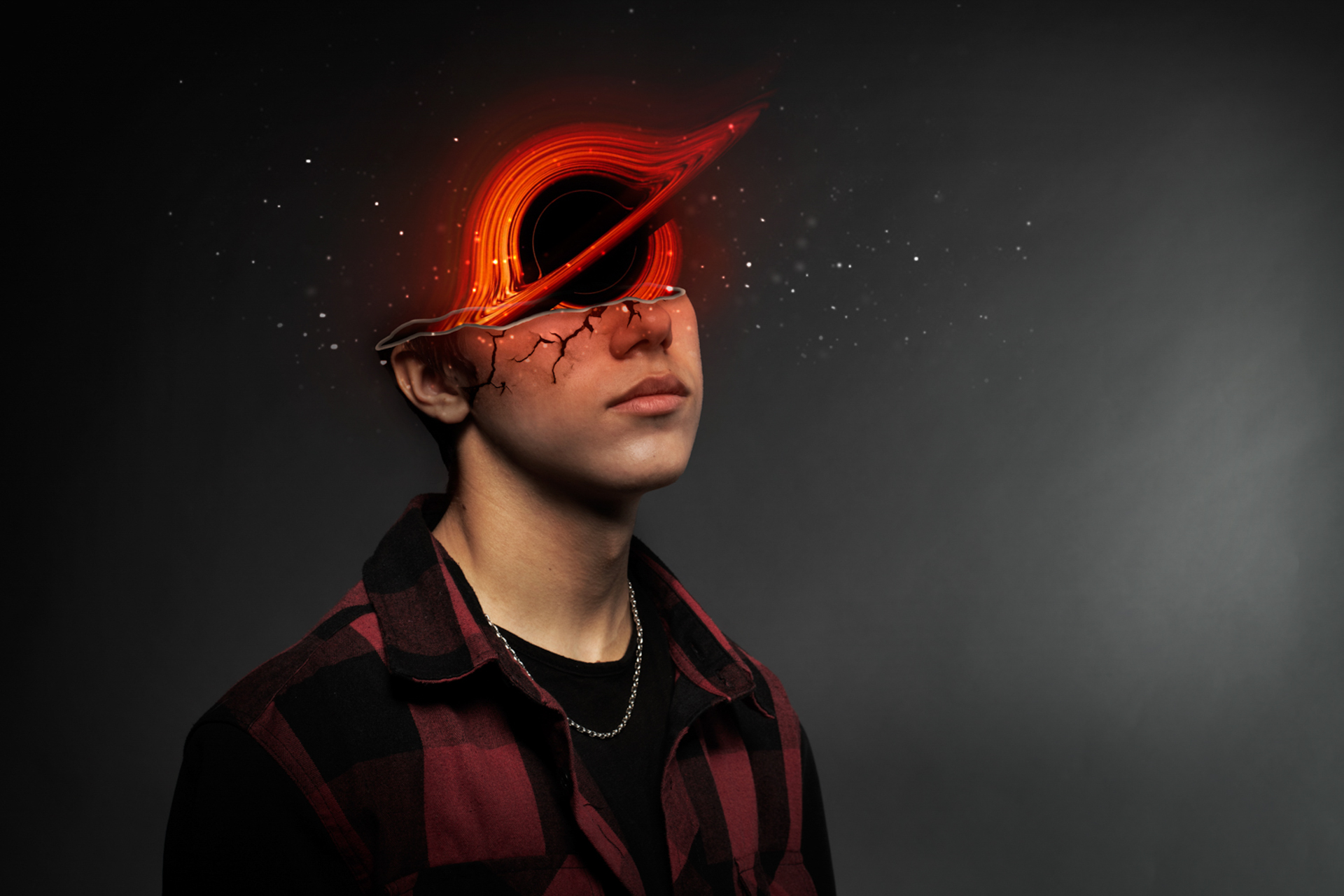 This photo depicts a man with half his face cut off, sliced just below his eyes. Coming out of his head is a black hole with red and orange colours. He is also wearing a red flannel and stars around the top of his head.