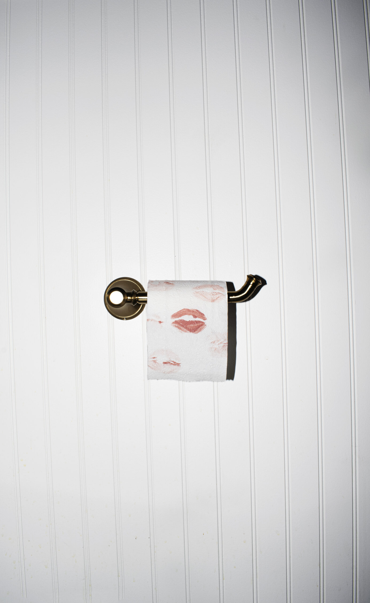 Photograph of a brass toilet paper holder with pink lipstick spots on the roll.