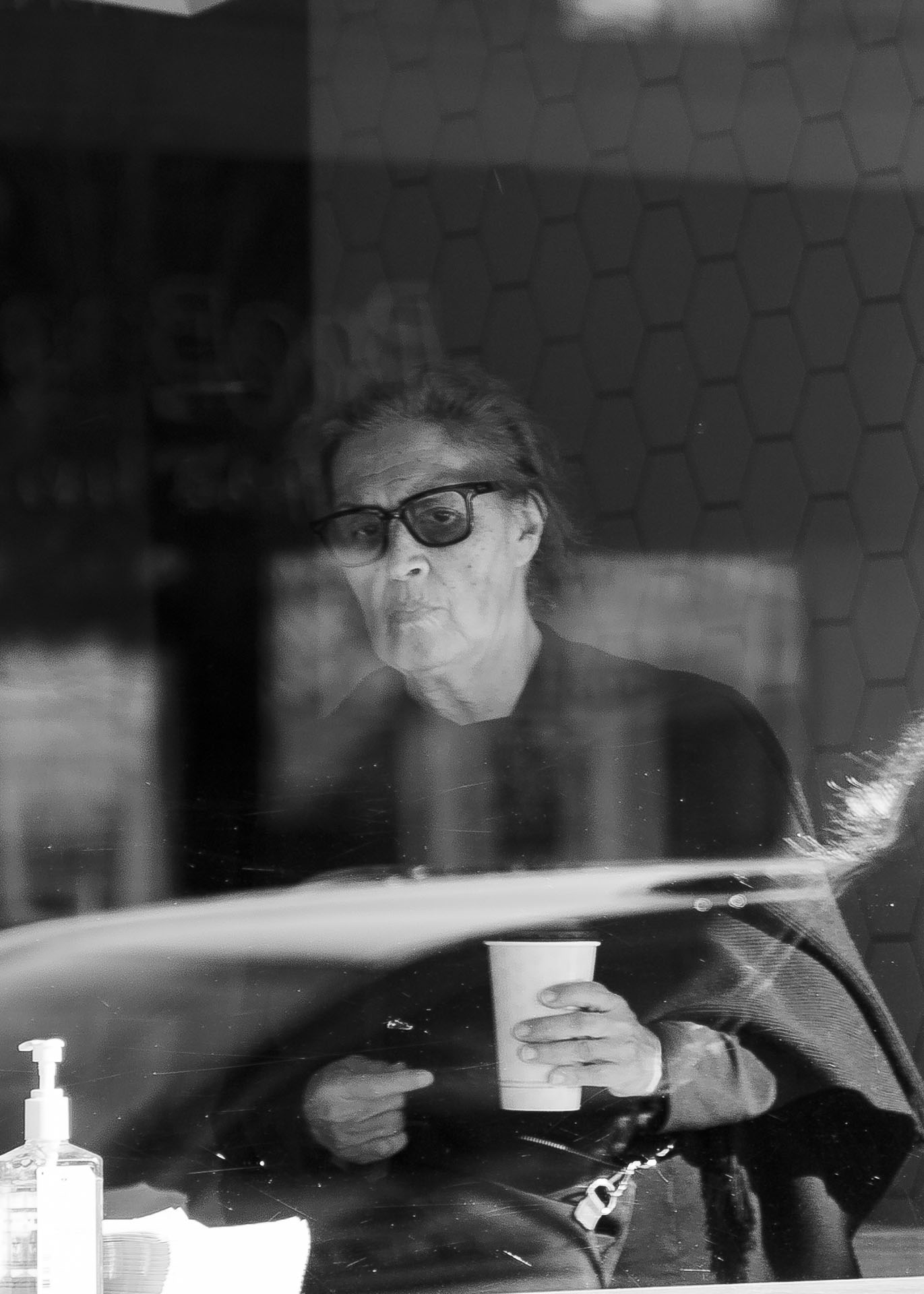 black and white image of a person grabbing a cup of coffee shot through a window