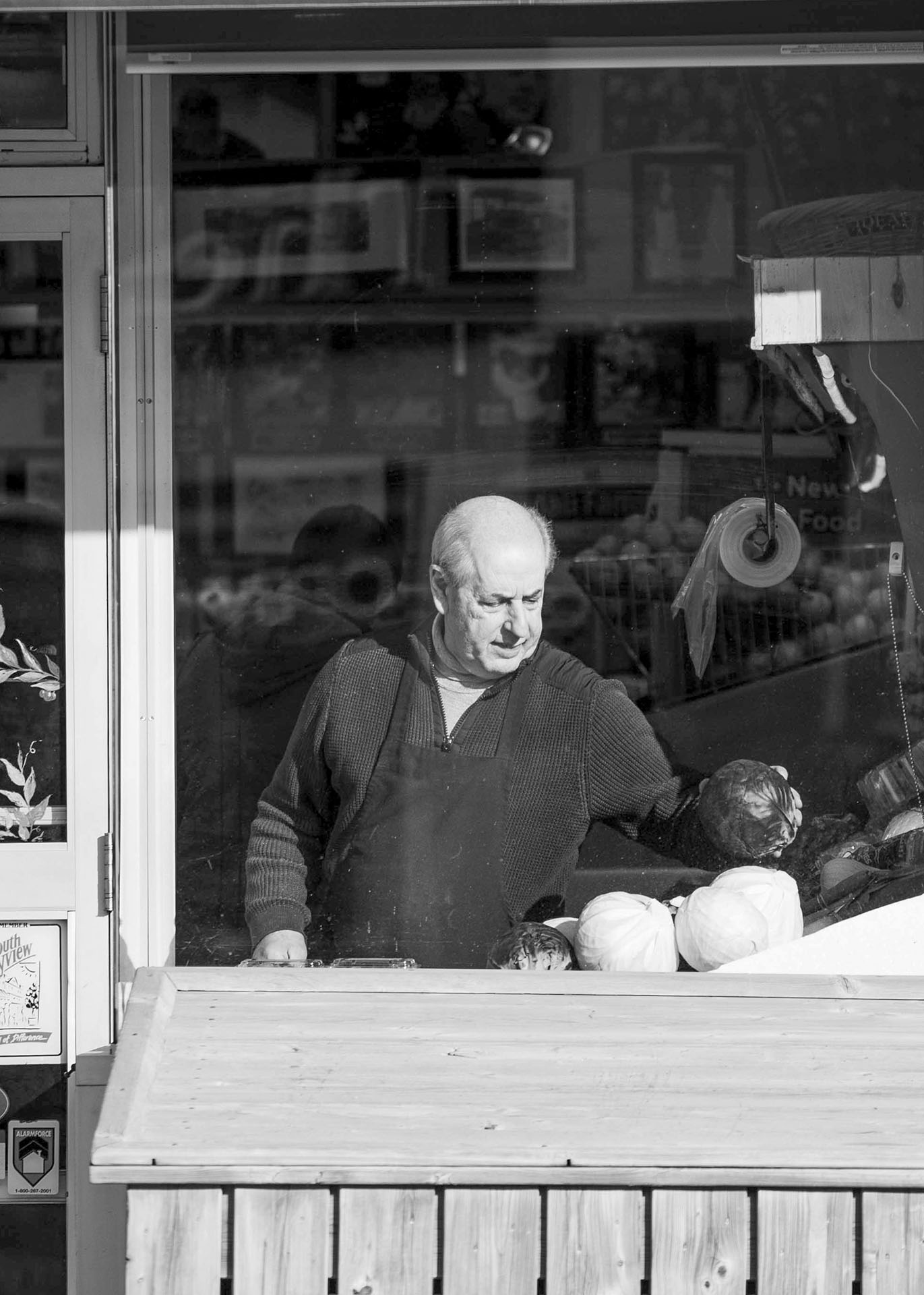 black and white image of an employee restocking vegetables show through a window