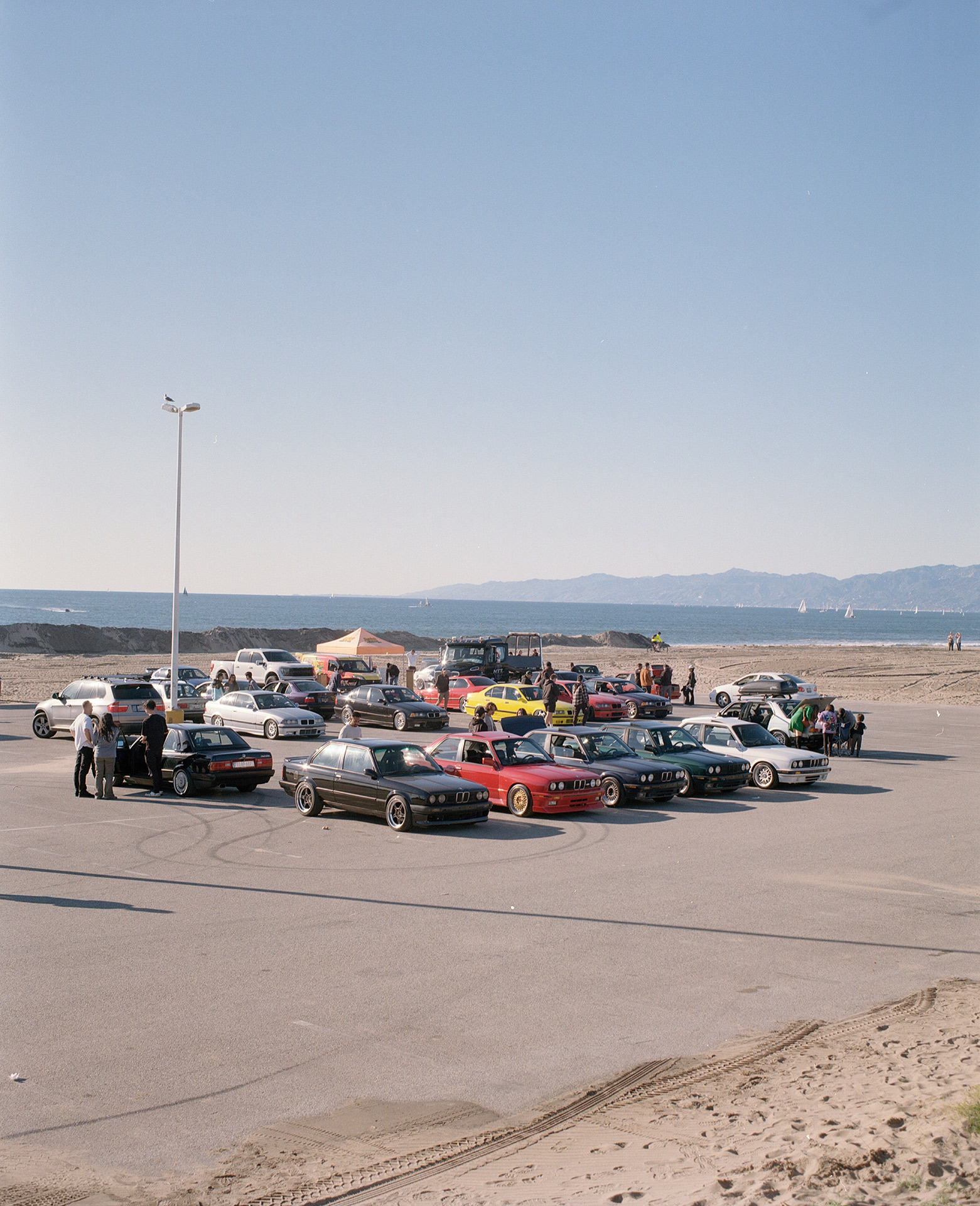 Cars parked in a parking lot right by the beach on a sunny day.