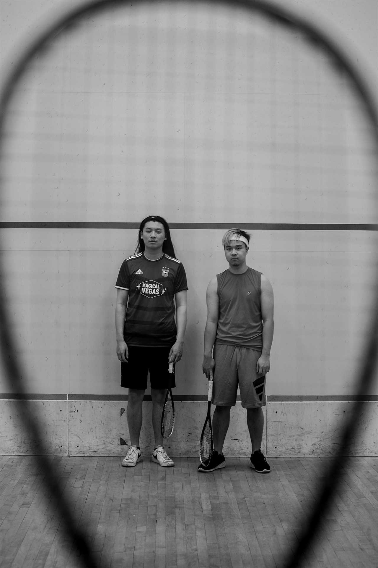Squash: My homies Aaron and Mark looking deadpan into the camera on a squash court while the camera peers through a squash racket