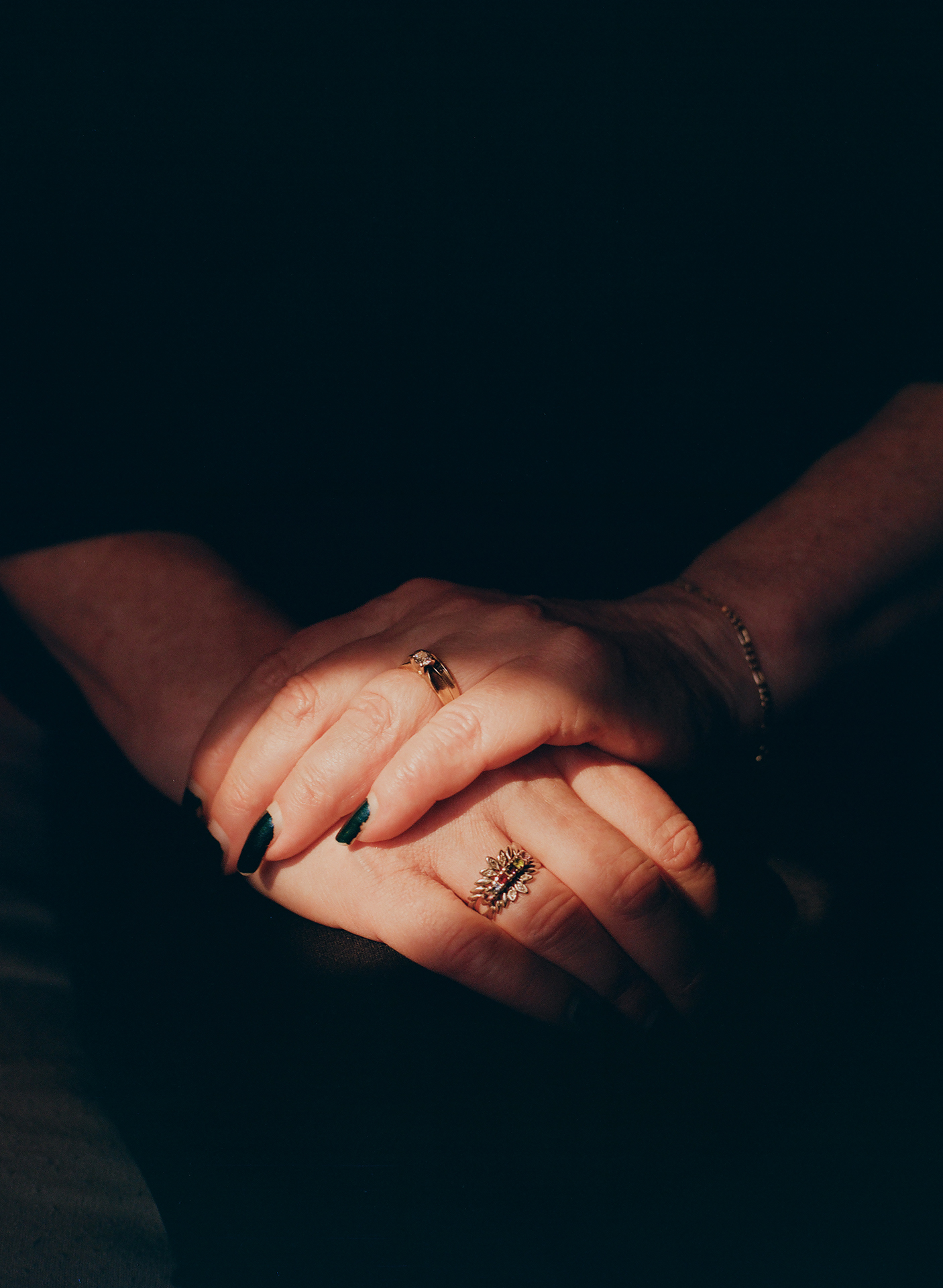 A mother's hands crossed over one another on her lap, the lighting showcasing her wedding bands.