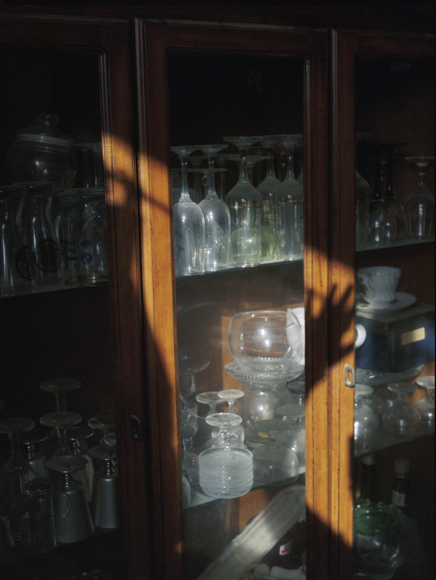 A reflection and shadow of a hand in the evening sunlight as it lays over a glass cabinet containing wine glasses.