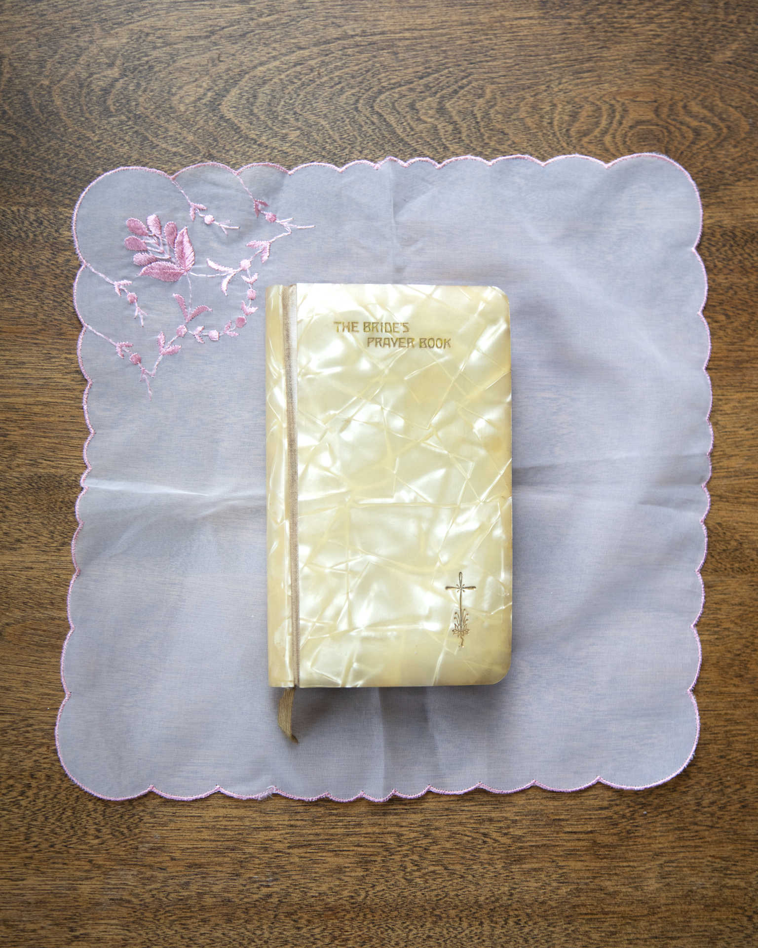 Gram's Bible: A small yellow book titled " The brides bible" sits on top of a white doily with pink trim, which is on a wooden table.