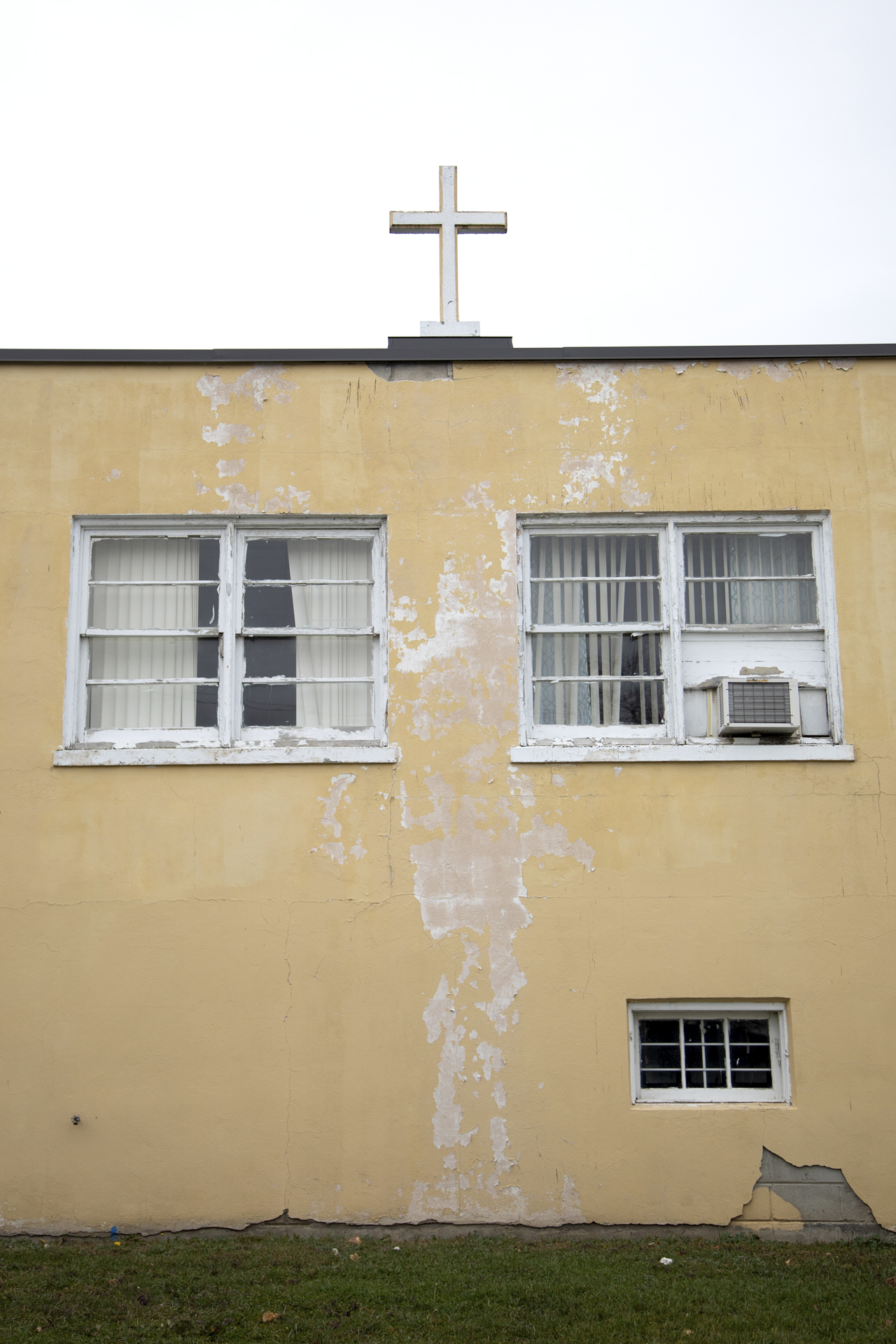 An old beige building with a cross on the roof. The wall is cracked and decaying.