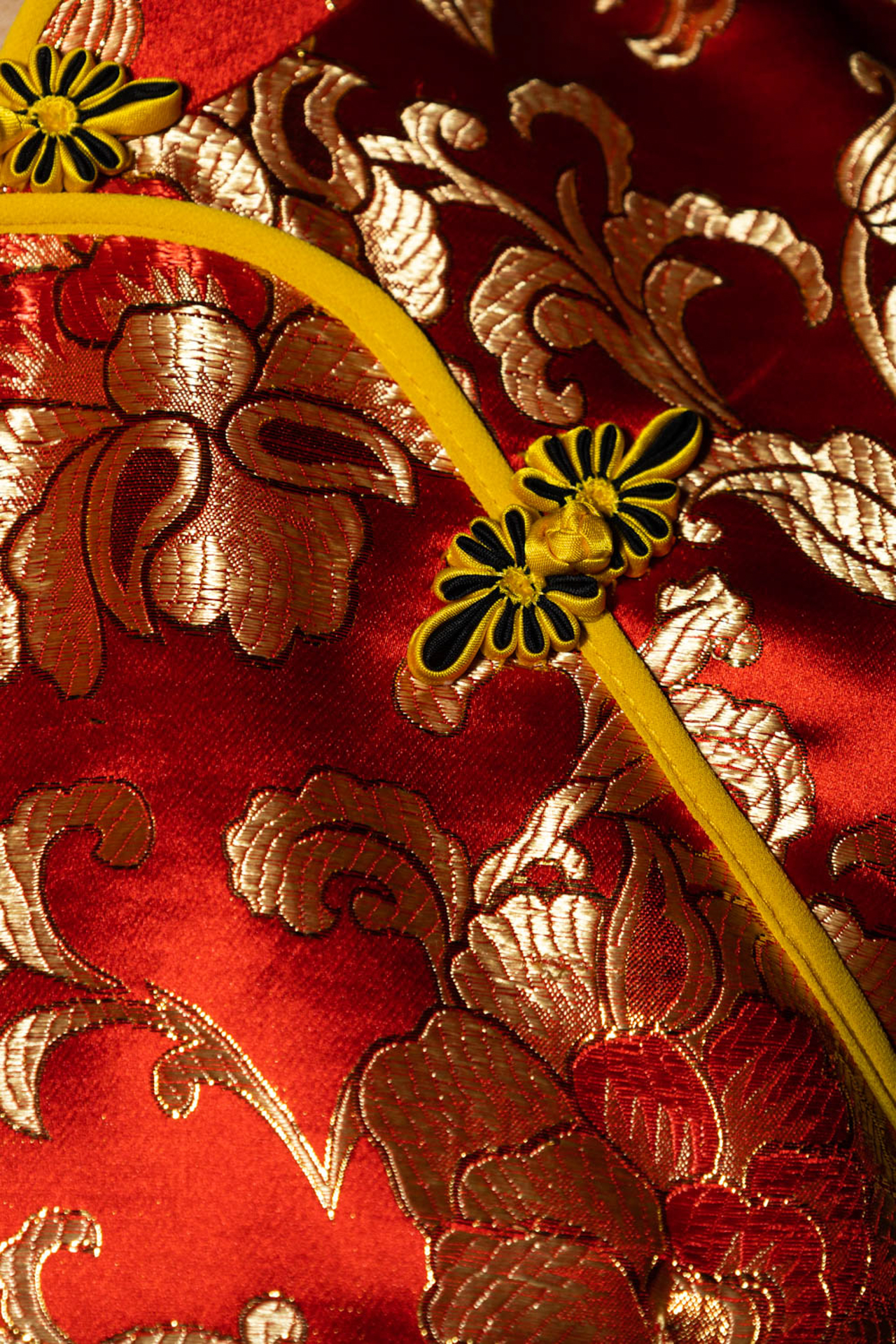 A detailed shot of traditional red qipao, there are various embellishments and embroidery featured throughout the photograph. The embroidery on the garment is shiny and catches your eye.
