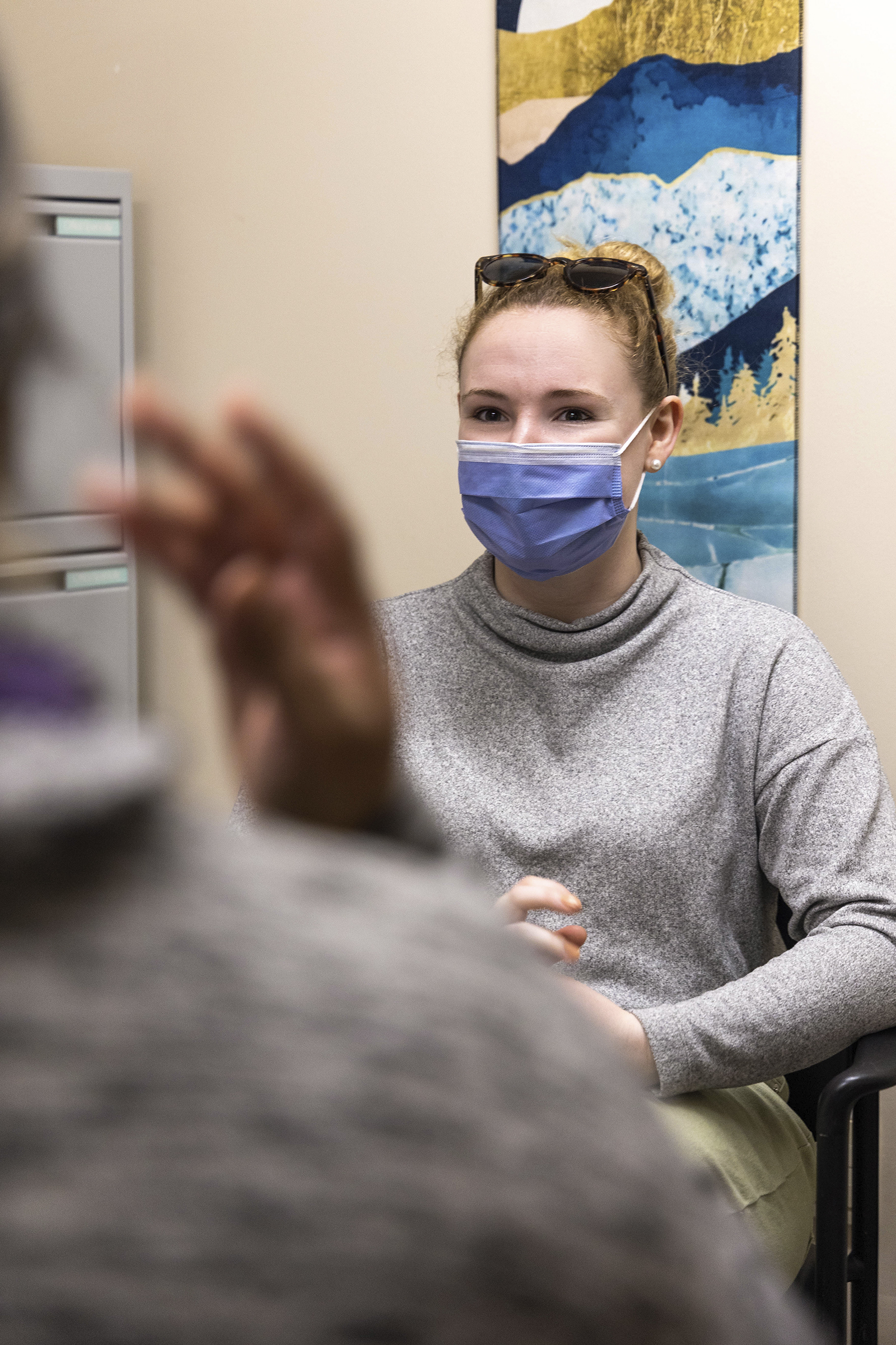 A woman, Laura, with a face mask on in her therapist's office, talking emotionally to her therapist. Laura is in focus and is shown over her therapist's blurred shoulder.
