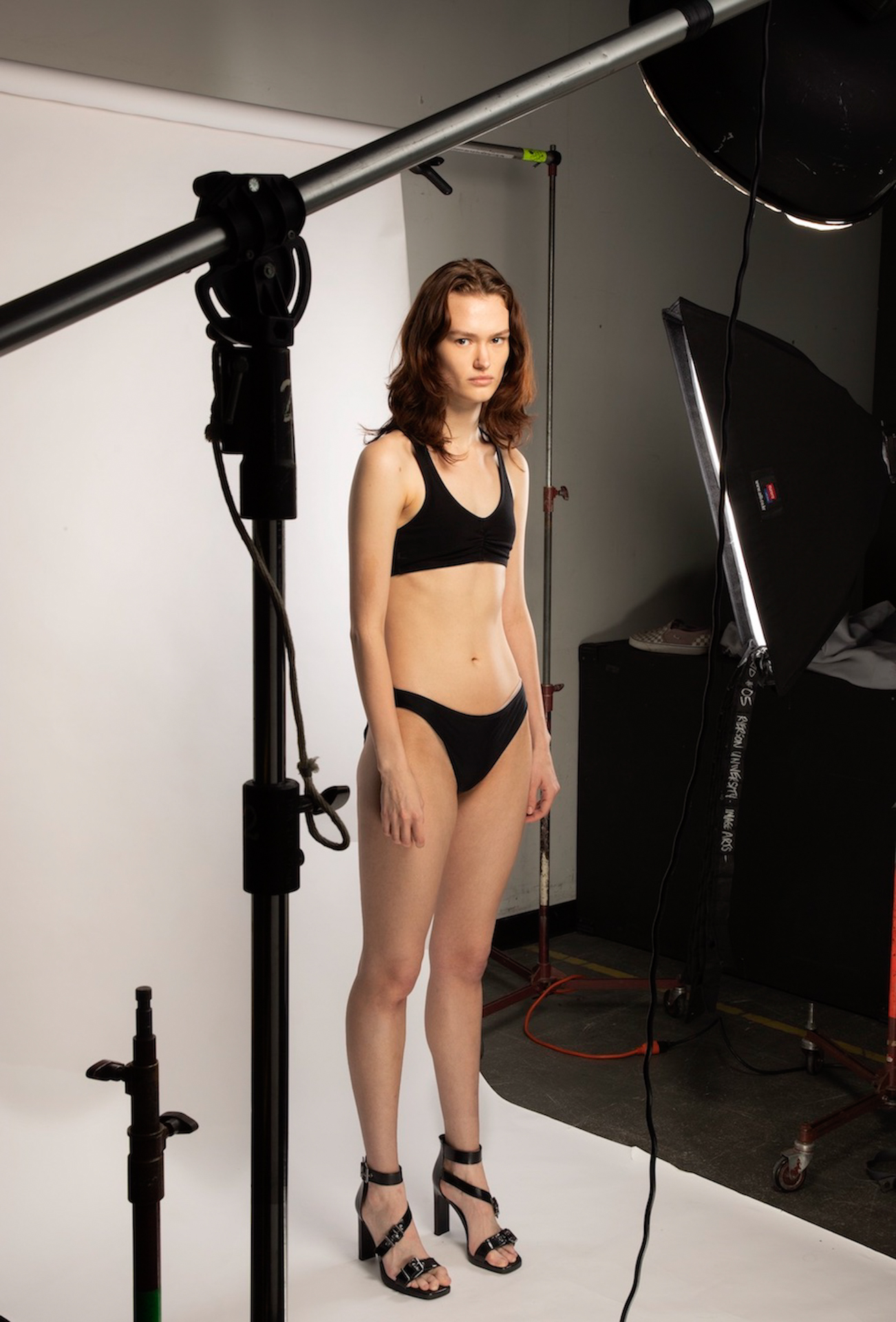 eve_hanno_thirdyearshow A women standing on a photo shoot set in her bra and underwear, she directly stares into the camera whilst being surrounded by various lights