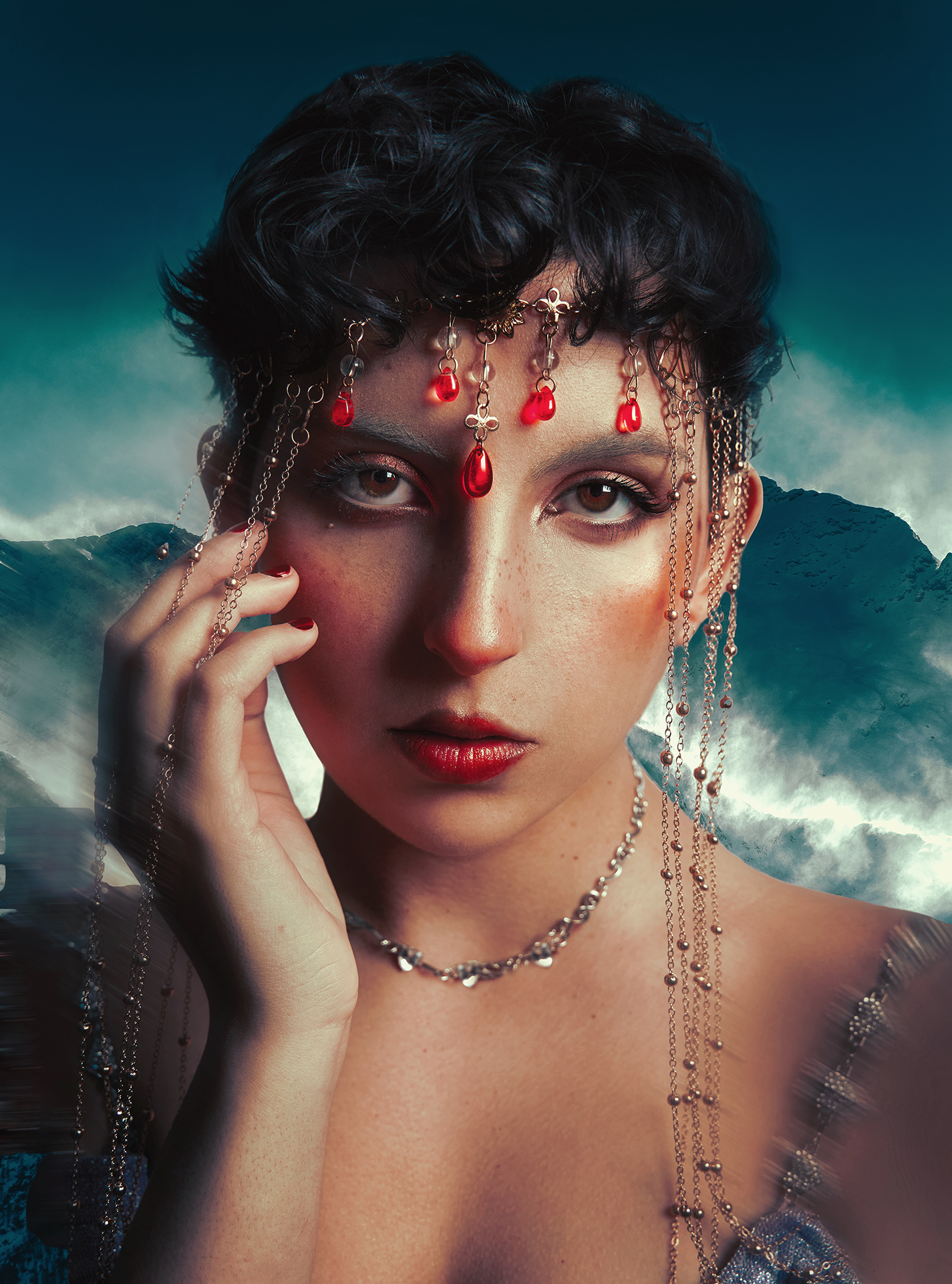 A close-up photo of a woman adorned with a red-jeweled headpiece. In the background is a blue mountainscape. There is motion-blur around her. She is strong and powerful.
