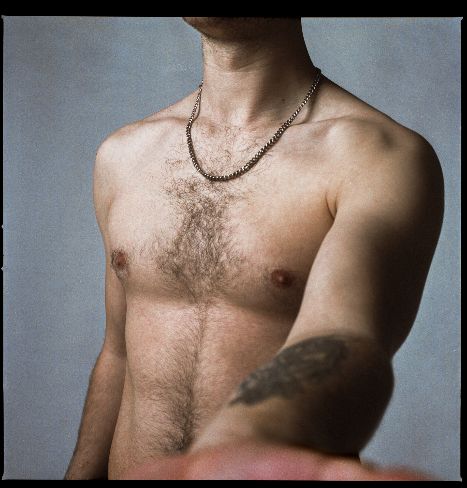 The image depicts a shirtless caucasian man with tattoos, grasping out to the camera as the figure (face not shown) confronts the lens.
