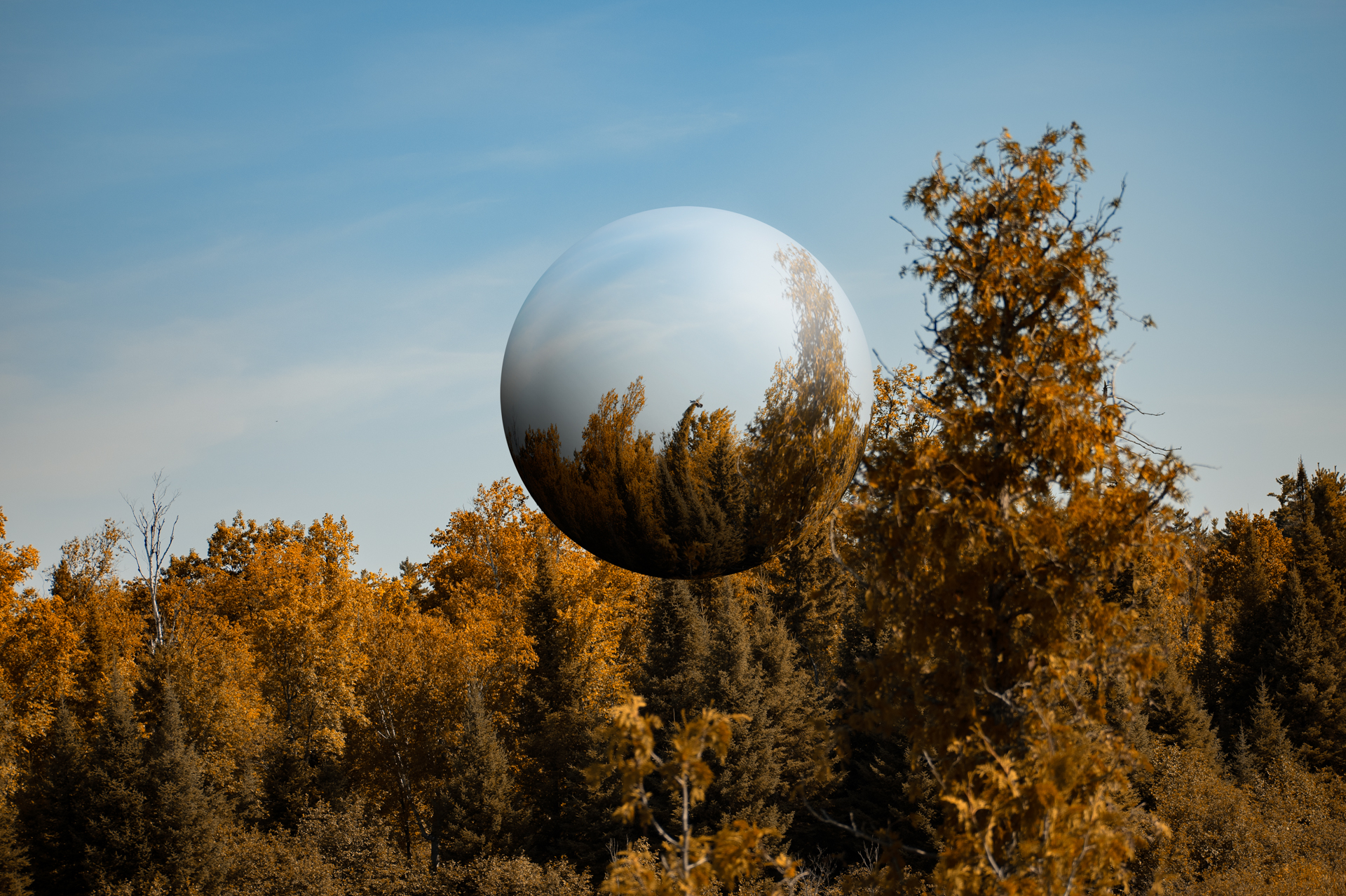 Landscape image of autumn trees and blue sky with a sphere floating in the middle.