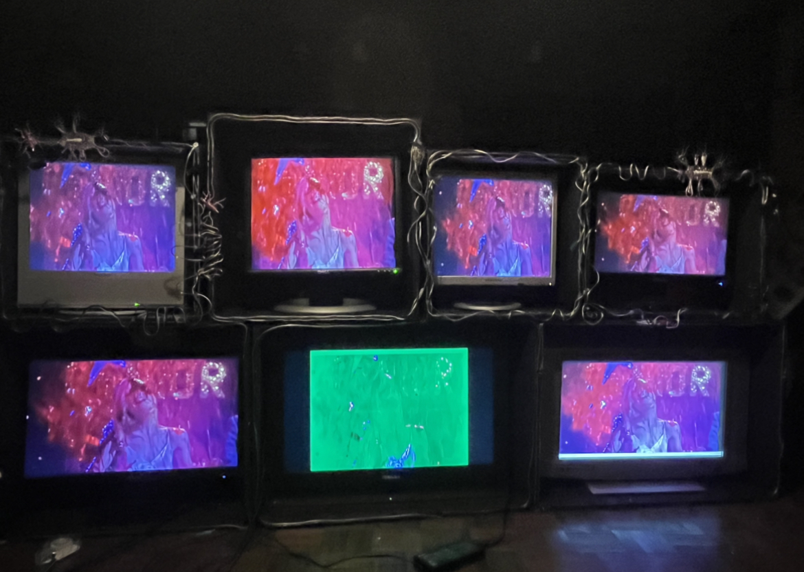 This image shows the structure which holds 7 monitors of all different sizes, decorated with scrap wires and the previously mentioned neurones. The monitors are displaying a still visual from Carrie 1978