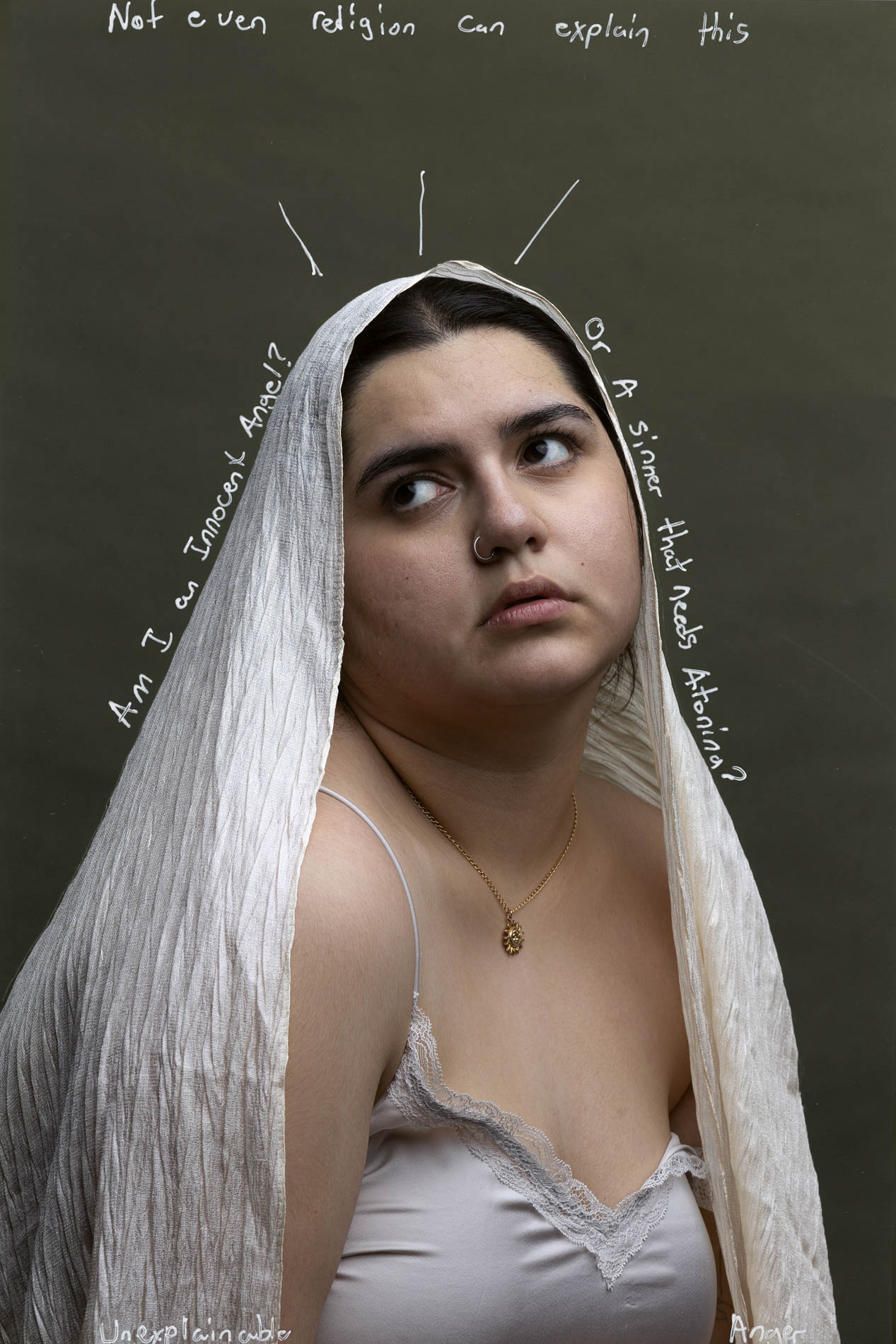 The photo features a young woman who is wearing a off-white veil on the top of her head and a white dress with lace, in front of an olive-green backdrop. She is looking to the side with a sad expression. There is white text on top of the image that reads “not even religion can explain this”, text that surrounds her figure that reads”am I an innocent angel?” On one side and “or a sinner that needs atoning” on the other side, as well as text on the bottom of the image that said “Unexplainable Anger”