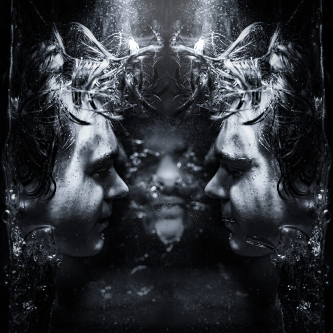 A black-and-white surreal portrait featuring a person submerged in water, their face mirrored and distorted.